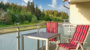 A balcony with a table and two striped chairs, overlooking a forested area. - GRA-211 - Large 2-room apartment with whirlpool - Residence Grafenmatt 2.2 (Feldberg (Schwarzwald))