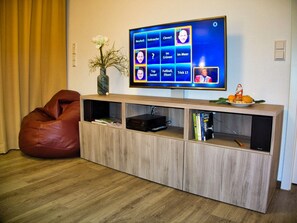 Un salon moderne avec un téléviseur à écran plat, un fauteuil en forme de poire rouge, un meuble de rangement en bois et une petite plante.