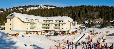 A ski resort with a large building, ski slopes, and a crowd of people.