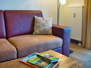 Un salon avec un canapé, une table basse avec des magazines, une lampe et un radiateur.
