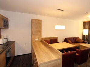 Une cuisine moderne avec des meubles en bois, un coin repas doté d’une table en bois et de chaises en cuir, ainsi qu’un luminaire suspendu.