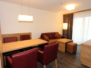A modern hotel room with a wooden dining table, red upholstered chairs, a brown sofa, and a wooden cabinet. - GRA-216 - Apartment with whirlpool and view of the slopes - Grafenmatt Residence (Feldberg (Schwarzwald))