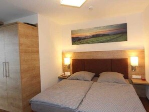 Une chambre à coucher comprenant un lit, deux tables de chevet, une commode, une armoire et un tableau accroché au mur.