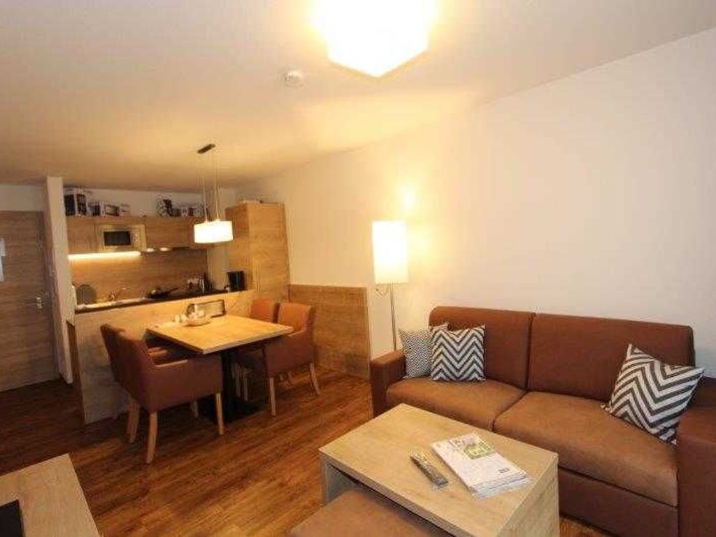 Un espace de vie compact comprenant un coin cuisine, un coin repas et un espace détente avec un canapé et une table basse.