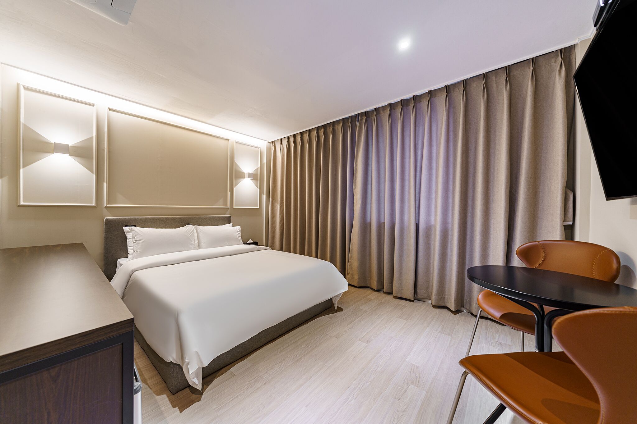 A hotel room with a bed, bedside tables, a desk, a chair, and a TV.