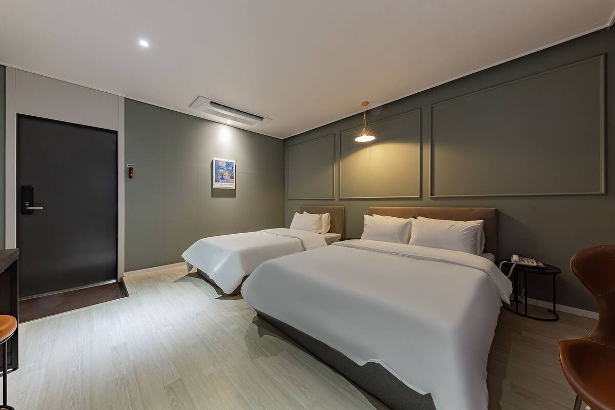 A hotel room with two beds, a desk, a chair, and a bedside table with a phone.