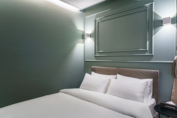Una cama bien hecha con sábanas blancas en una habitación con paredes verde azulado y un cabecero sencillo.