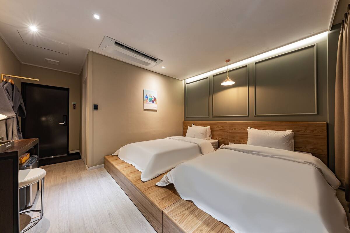 A hotel room with two beds, a desk, a chair, and a mirror.