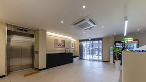 A modern hotel lobby with a reception desk, an elevator, and a Coca-Cola refrigerator. - Brown Dot Hotel (Jecheon)