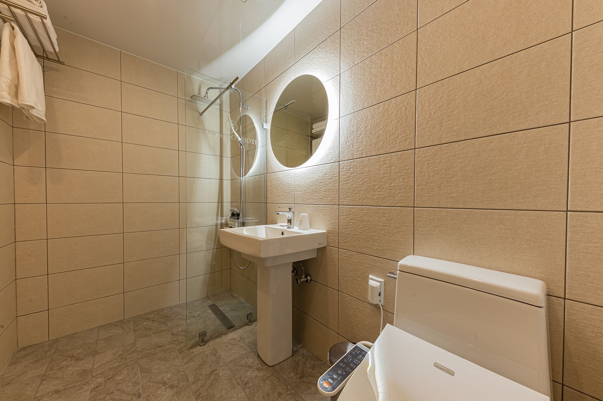 A modern bathroom with a pedestal sink, a toilet with a control panel, and a shower area.