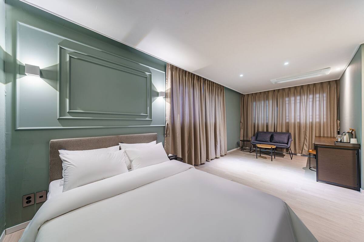 A hotel room with a large bed, a desk, a chair, and a sofa.