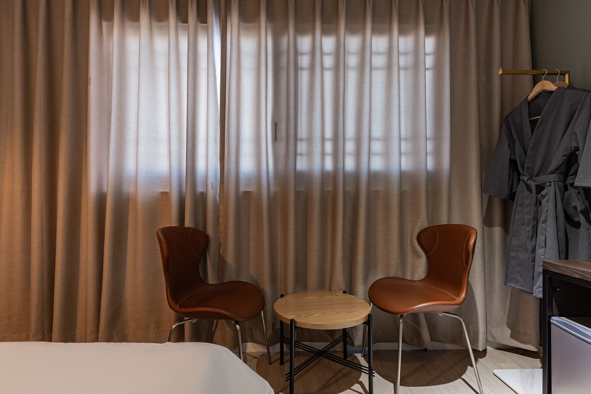 Une chambre d’hôtel avec un lit, deux chaises, une petite table ronde et un peignoir suspendu à un porte-manteau.