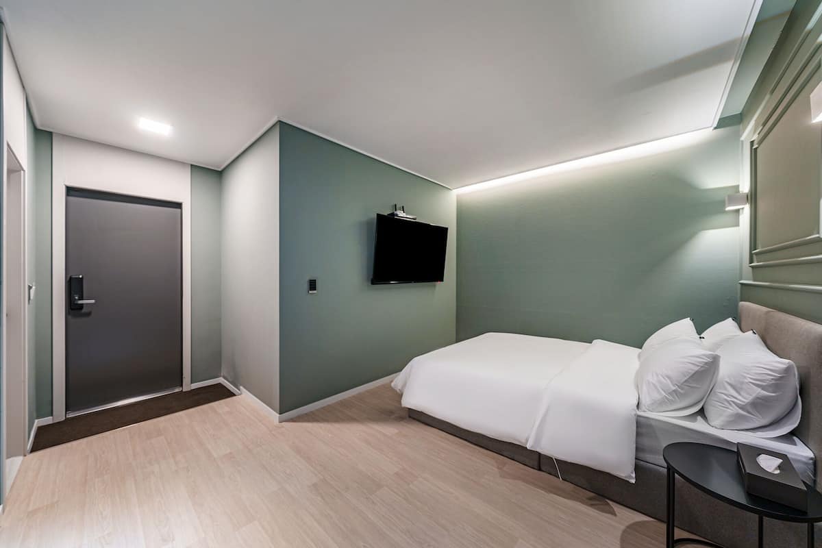A modern hotel room with a bed, a TV mounted on the wall, and a door.