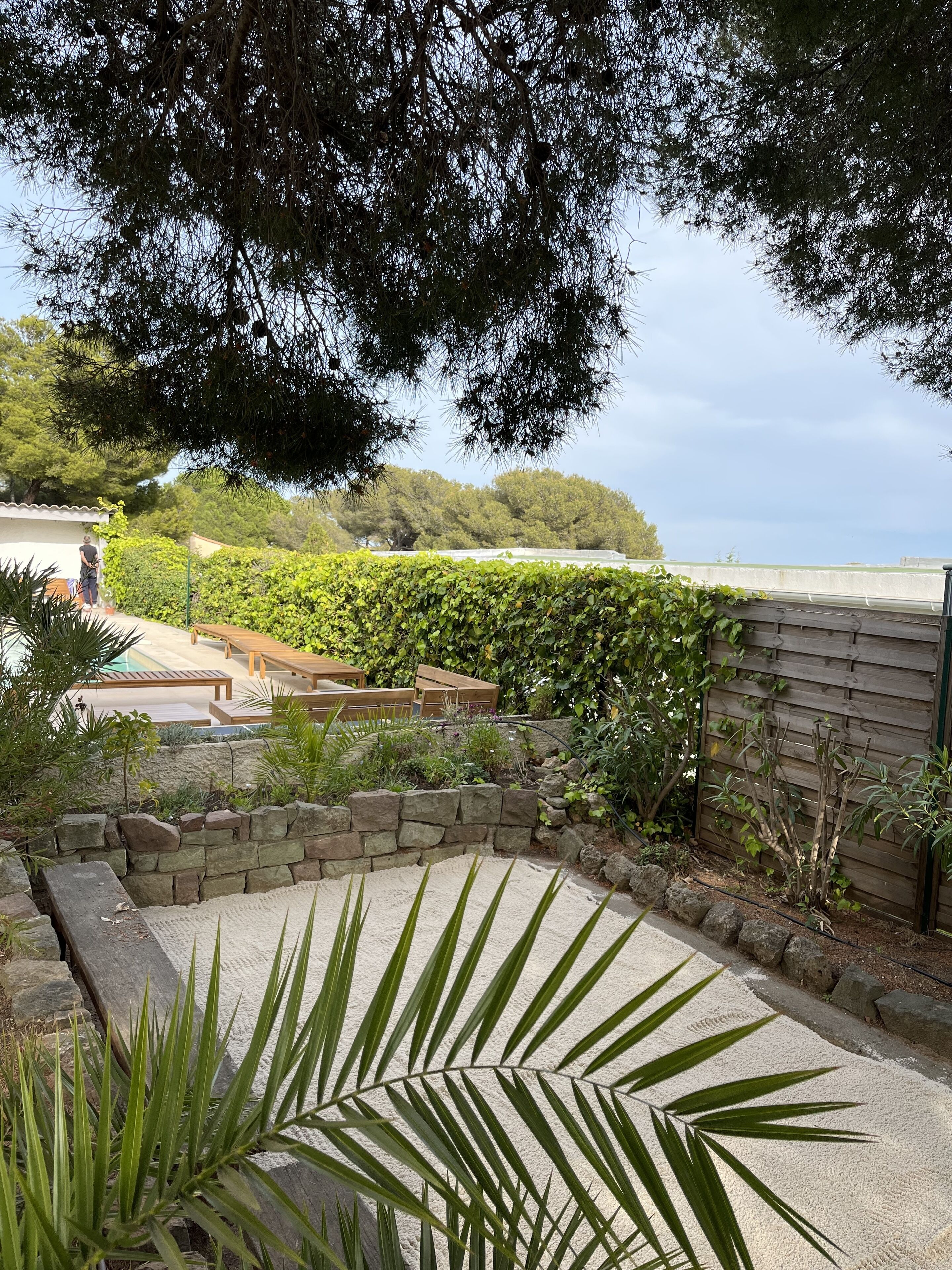 Un jardín con muro de piedra, terraza de madera y piscina.