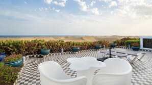 Une terrasse dotée d’un sol à carreaux, de fauteuils blancs et de plantes en pot, offrant une vue sur un paysage désertique.