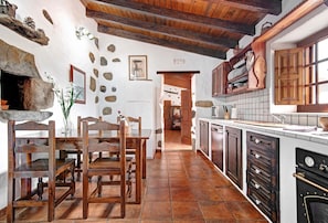 A rustic kitchen with stone walls, wooden beams, and a tiled floor.
