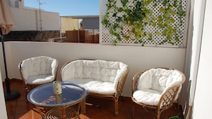 A terrace with wicker furniture, a glass table, and a decorative wall.