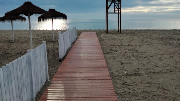 A wooden boardwalk leading to a beach with a lifeguard tower and thatched umbrellas.