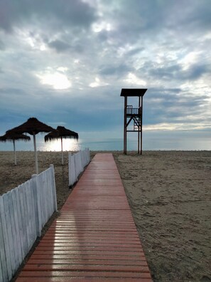 A wooden boardwalk leading to a beach with a lifeguard tower and thatched umbrellas. - 'El Rinconcito de Rosa' Apartment with Wi-Fi & AC, Perfect for Couples (Nerja)