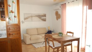 A living room with a sofa, wooden dining table, chairs, a lamp, and a wall-mounted air conditioner.