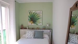 A bedroom with a bed, pillows, a bedside table, a lamp, and a wall painting.