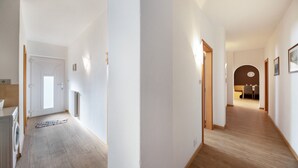 Un corridoio con pavimento in legno, pareti bianche e una porta che dà su una stanza.