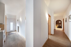 A hallway with a wooden floor, white walls, and a door leading to a room.