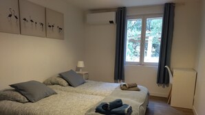 Een slaapkamer met een groot bed, een nachtkastje, een lamp, een raam met gordijnen en een wandairconditioner.