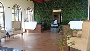 A reception area with a green wall, two reception desks, and a statue. - The Pench International (Kurai)