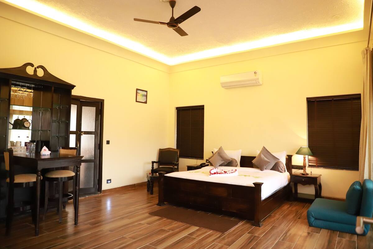 A hotel room with a bed, a desk with chairs, a ceiling fan, and a window with curtains.