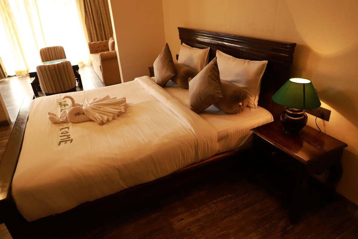 A neatly made bed with a towel and a pillow with "LOVE" embroidered on it, a bedside lamp, and a wooden nightstand.