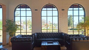 A spacious room with a black leather sofa, a wooden coffee table, and large arched windows offering a view of the outdoors. - The Pench International (Kurai)
