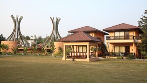 A hotel with a covered outdoor seating area, a pool, and a distinctive curved architectural feature in the background. - The Pench International (Kurai)
