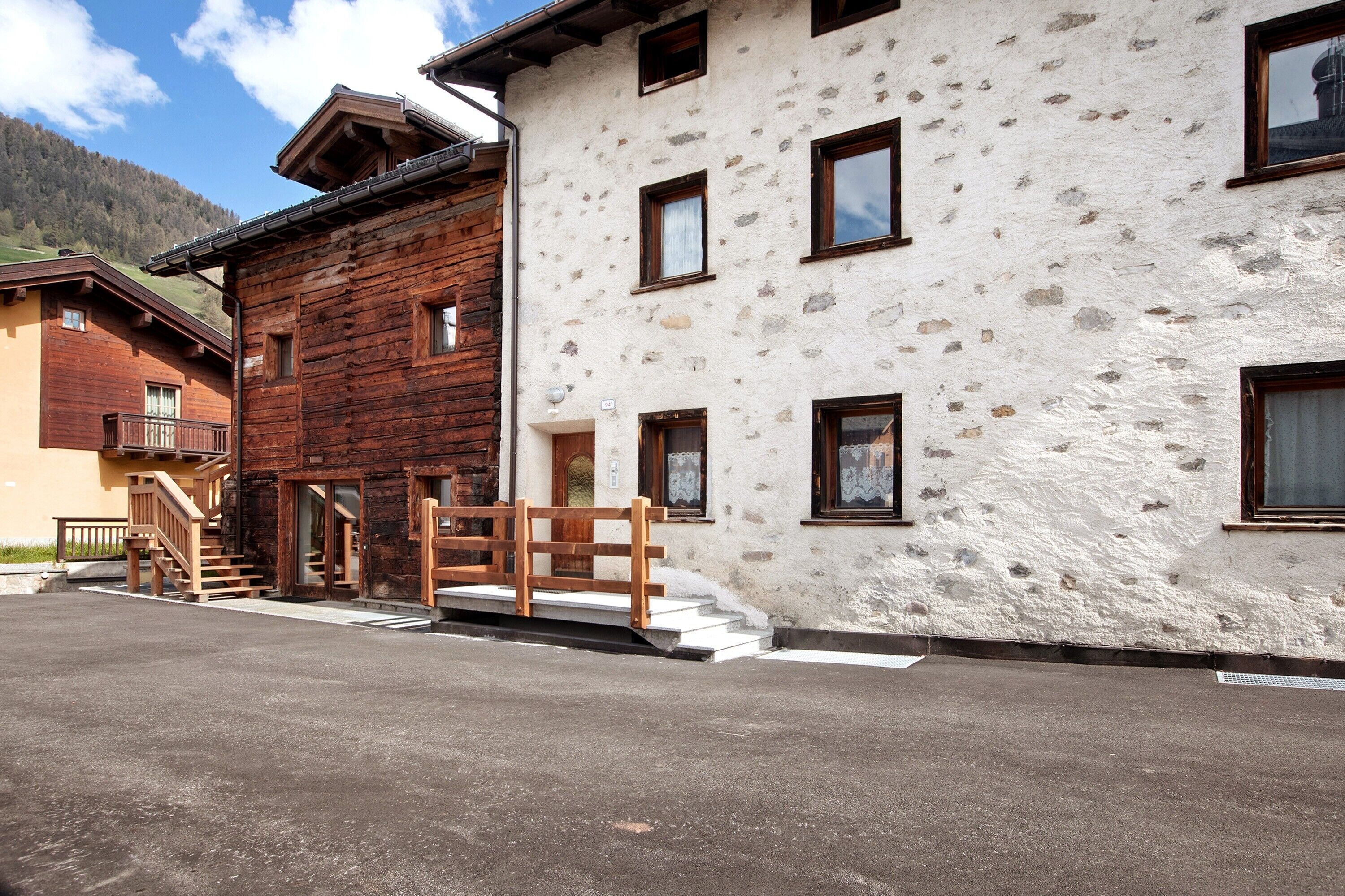 Un edificio a due piani con facciata in legno e parete in pietra, una scala e un piccolo balcone.