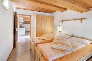 Un dormitorio con cama de madera, un armario y una pequeña cocina en el fondo.