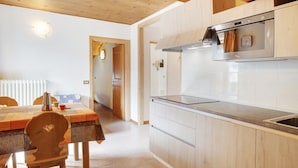 A kitchen with wooden cabinets, a stainless steel oven, and a dining area with a table and chairs.