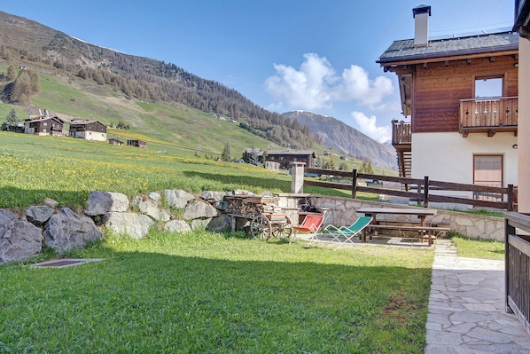 A mountain house with a stone pathway, wooden deck, and a view of the surrounding hills.