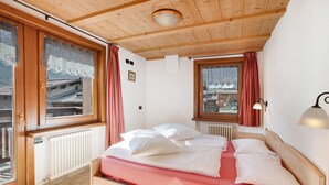 Ein Schlafzimmer mit einem hölzernen Bett, einem Fenster mit Vorhängen, einem Heizkörper und einer Lampe.