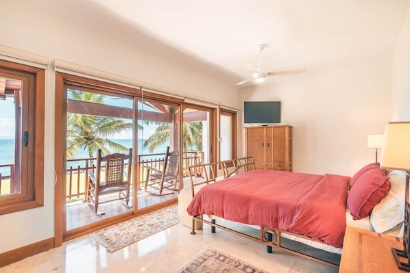A bedroom with a bed, a TV, and a view of the beach.
