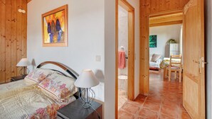Een slaapkamer met een bed, bedlampen, een schilderij en een houten deur die naar een andere kamer leidt.