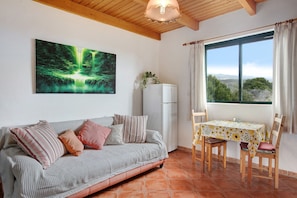 A room with a sofa, a table with chairs, a refrigerator, a window with curtains, and a painting on the wall.