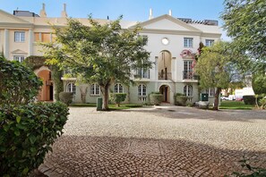 Un edificio grande con un patio empedrado, puertas en arco y un balcón lleno de flores.