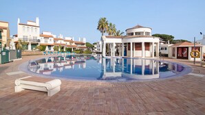 A swimming pool with a circular design, surrounded by a tiled deck, and adjacent to a building with a dome-like structure. - Apartment 'Old Village T2 Duplex' with Shared Pool, Wi-Fi and Air Conditioning (Quarteira)