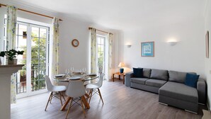 A dining area with a glass table and chairs, a sofa, and a lamp. - Apartment 'Old Village T2 Duplex' with Shared Pool, Wi-Fi and Air Conditioning (Quarteira)