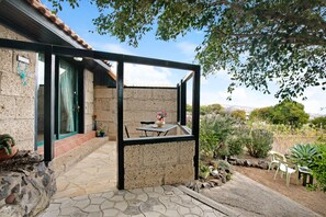 A patio with a table and chairs, a stone wall, and a view of the surrounding landscape. - Apartment "Casa Munay" with Sea View, Terrace & Shared Garden (Granadilla de Abona)