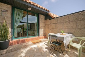 A patio with a table and chairs, a potted plant, and a stone wall. - Apartment "Casa Munay" with Sea View, Terrace & Shared Garden (Granadilla de Abona)