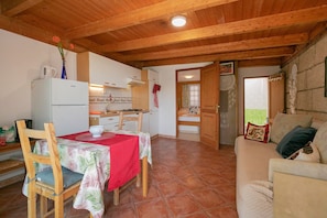 A cozy kitchen with wooden beams, a dining table with chairs, a refrigerator, and a sofa in a living area.