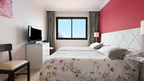 Une chambre à coucher avec un lit, un bureau avec une télévision, une chaise et une fenêtre avec des rideaux.