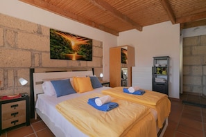 Un lit double avec deux oreillers, une table de chevet avec une lampe, un miroir, une étagère avec des serviettes et un tableau au mur.