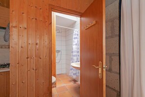 Une porte en bois donne accès à une salle de bain équipée d’une douche, de toilettes et d’un lavabo.